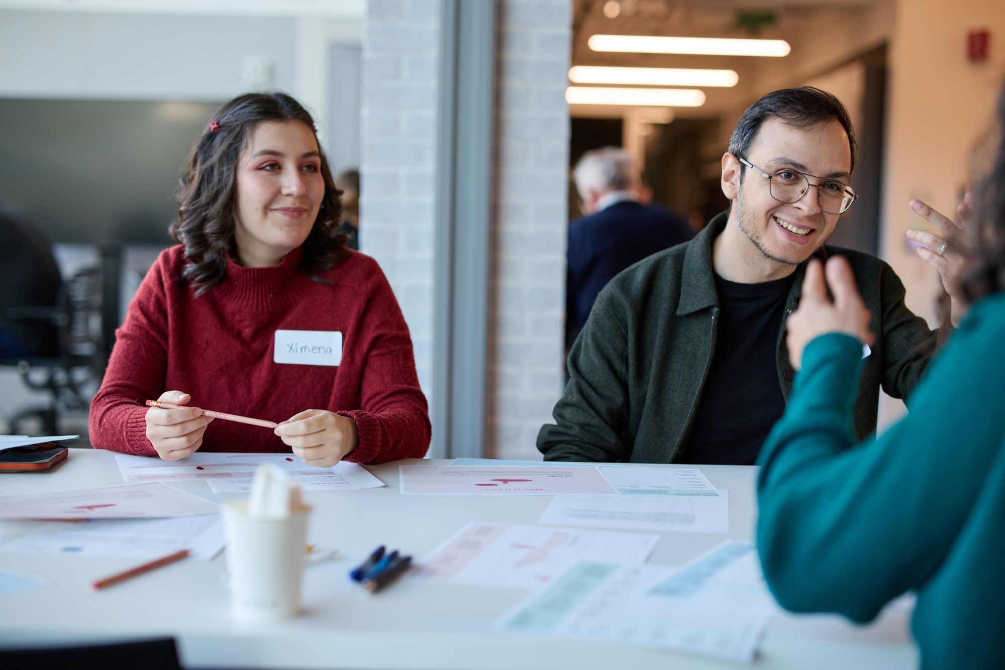 Two attendees at a table smile as they listen to another group member speak.